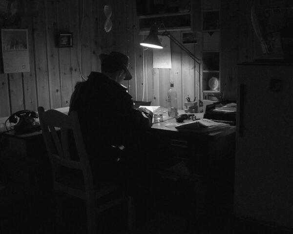 Private investigator engaged in investigative note writing under a desk lamp in a dimly lit office.